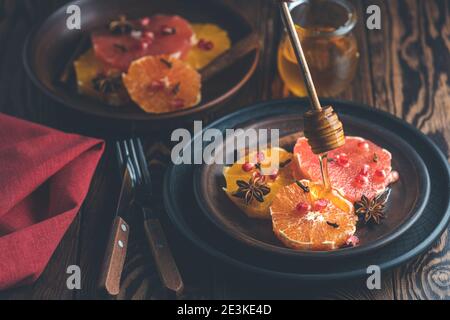 Orangefarbenes Dessert mit Weinhonig oder Ahorn-Sirup und Ingwer-Gewürz, verzierten Granatapfelbeeren. Wunderbar süße, reiche und frische Speisen. Dunkles, rustikales Bac Stockfoto