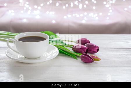 Eine Tasse Kaffee und Tulpen auf einem hellen Hintergrund mit brennenden Lichtern. Stockfoto