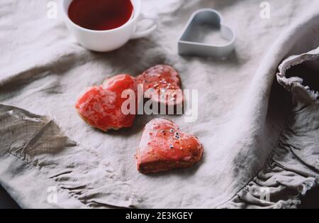 Herzförmige rote handgemachte Kekse und Hibiskustee in weißer Tasse und Lichter. Valentinstag-Konzept. Stockfoto