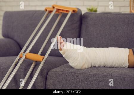 Die Krücken und das gebrochene Bein in der Gipsbandage des Unbekannten liegend und ruhend auf dem Sofa. Stockfoto