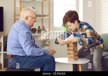 Großvater und Enkel spielen eine Partie Jenga und ziehen abwechselnd Steine aus einem hölzernen Turm. Stockfoto