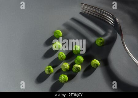 Harte Ernährung mit ein paar grünen Erbsen und eine Gabel mit Schatten auf einem grauen Hintergrund mit Kopierraum, moderne abstrakte Konzept für die Auflösung vegetarisch zu essen Stockfoto