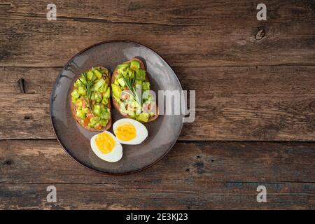 Zwei Avocado-Sandwiches und in Scheiben geschnittene gekochte Eier auf Holzgrund. Stockfoto