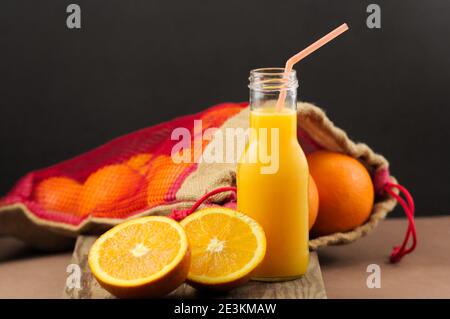 Stillleben einer Glasflasche mit Orangensaft neben anderen Stücken von ganzen Früchten und in der Hälfte geschnitten, mit einem schwarzen Hintergrund und Kopierraum Stockfoto
