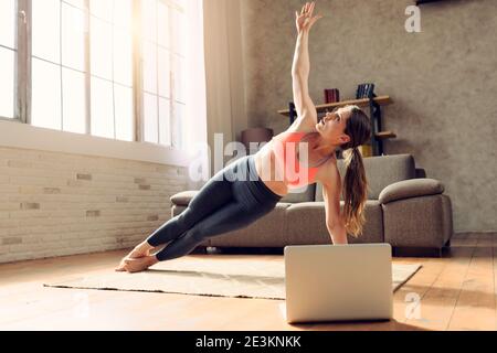 Junge Frau folgt mit einem Laptop ein Fitness-Studio Übungen. Sie ist zu Hause wegen Coronavirus codiv-19 Quarantäne Stockfoto