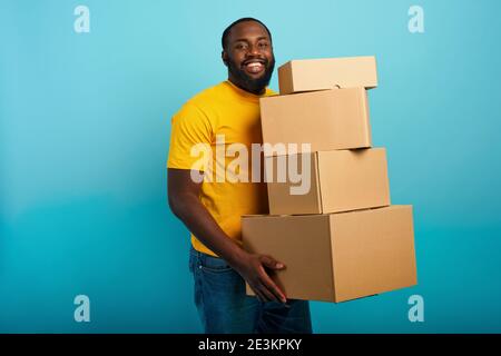 Glücklicher Mann hält eine Menge empfangene Pakete. Cyanfarbener Hintergrund Stockfoto