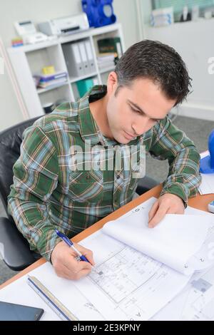 Mann saß am Schreibtisch und arbeitete an Maßstabszeichnungen Stockfoto