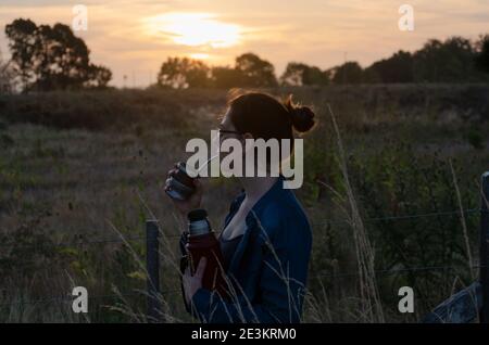 Mädchen beobachten den Sonnenuntergang und trinken Mate auf dem Land Stockfoto