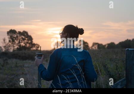 Mädchen beobachten den Sonnenuntergang und trinken Mate auf dem Land Stockfoto