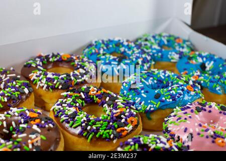 Donuts mit brauner, blauer, rosa und weißer Glasur, bedeckt mit bunten Streuseln in einer weißen Box auf einem Holztisch Stockfoto