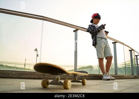 Teenage asiatische Skateboarder Junge Blick auf Handy während der Ruhe Stockfoto