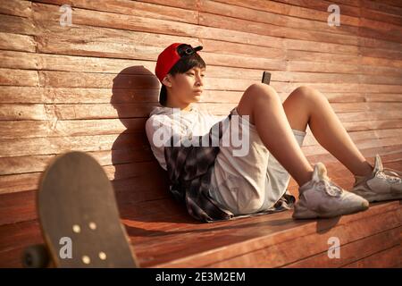 Teenage asiatische Skateboarder Junge Blick auf Handy während der Ruhe Stockfoto