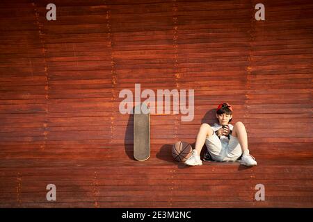 Teenage asiatische Skateboarder Junge Blick auf Handy während der Ruhe Stockfoto