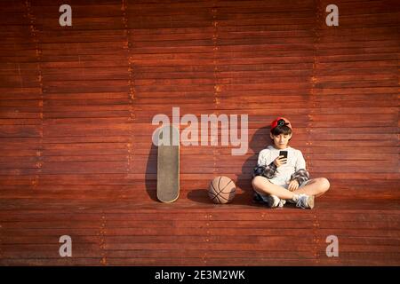 Teenage asiatische Skateboarder Kind Blick auf Handy während der Ruhe Stockfoto