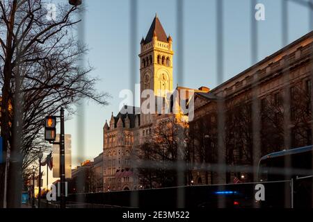 Washington, DC, USA, 19. Januar 2021. Im Bild: Der Turm des alten Postgebäudes, das heute das Trump Hotel ist, bei Sonnenuntergang durch den Sicherheitszaun gesehen. Die untergehende Sonne und eine Sekunde links auf dem Fußgängersignal schienen eine passende Metapher für die Trump-Regierung zu sein, die etwa 24 Stunden nach der Aufnahme des Fotos endet. Die Vorbereitungen und Sicherheitsmaßnahmen für die Amtseinführung von Joe Biden wurden viel früher als gewöhnlich eingeleitet, weil Trump-Anhänger, weiße VormachthaberInnen und andere Rechtsextremisten mit Gewalt drohten. Kredit: Allison C Bailey/Alamy Live Nachrichten Stockfoto