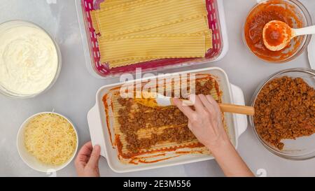 Rindfleisch Lasagne Schritt für Schritt Rezept. Lasagne zusammenbauen. Frau Hände verteilen Schicht von gebratenem Hackfleisch auf Nudeln Stockfoto