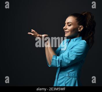 Junge Brünette Frau Arzt Krankenschwester in blauen medizinischen Kleid hält Ihre offenen Handflächen mit Kopierplatz vor ihr Gesicht Stockfoto
