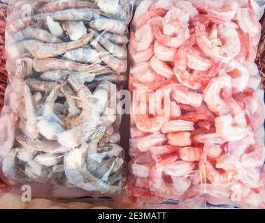 Zwei große Plastiktüten mit gefrorenen rohen und gekochten Garnelen, auf der Theke des Fischmarktes. Stockfoto