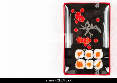 Frische appetitliche Brötchen mit Lachs in Nori-Algen in schwarz-roten Tellern auf weißem Teller. Blick von oben Stockfoto