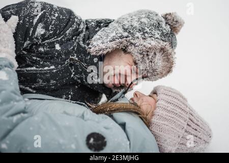 Liebevoller Kerl und Mädchen liegen im Schnee. Junge glückliche Paar zu Fuß im Winter Stockfoto
