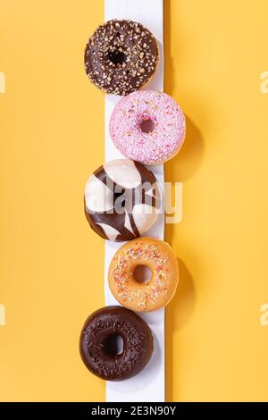 Flache Lay-Komposition mit gemischten Donuts auf gelbem Hintergrund. Vertikales Format. Stockfoto