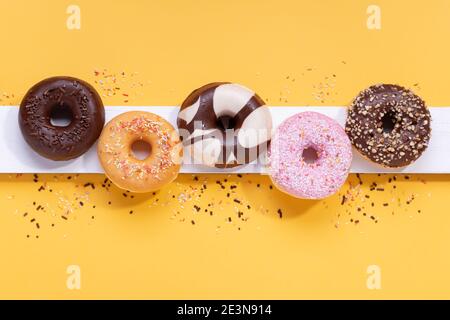 Flache Lay-Komposition mit gemischten Donuts auf gelbem Hintergrund. Stockfoto