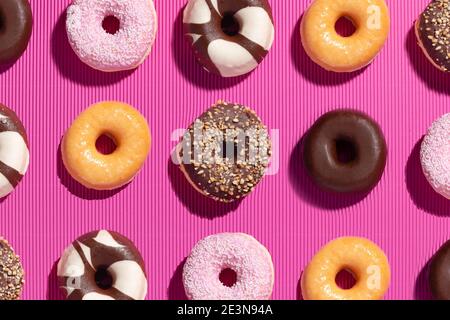 Flache Lay-Komposition aus gemischten Donuts auf rosa Hintergrund. Stockfoto