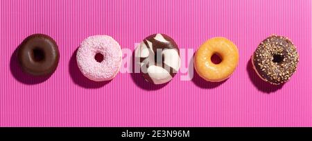 Flache Lay-Komposition mit gemischten Donuts auf rosa Hintergrund. Stockfoto