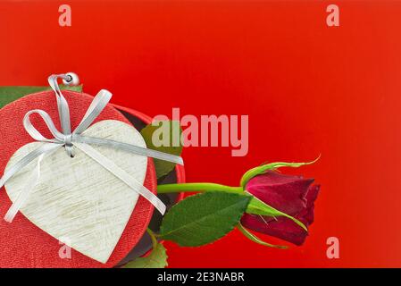 Einzelne Rose auf Geschenkbox und Herzmedaillon über rot Hintergrund mit freiem Kopierbereich Stockfoto