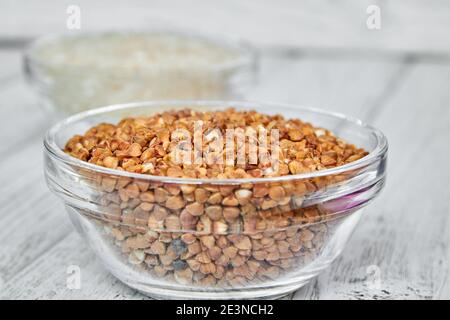 Roher weißer Reis und Buchweizengrundeln in einer transparenten Glasplatte auf Holzhintergrund. Nahaufnahme. Stockfoto