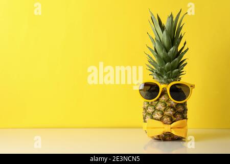 Lustige Ananas mit Fliege und Sonnenbrille auf gelbem Hintergrund, ein cooles tropisches Ananas-Party-Konzept Stockfoto