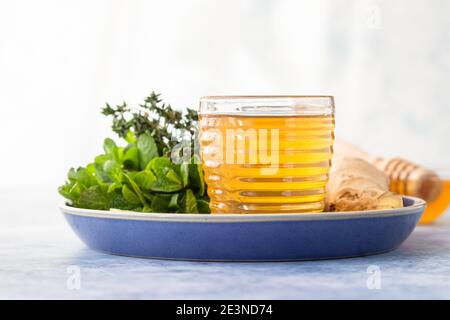 Eine Tasse frischen Kräutertee mit Thymian, Minze, Ingwer, Zitrone und Honig auf blauem Betongrund. Selektiver Fokus. Stockfoto