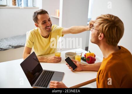 Glückliches schwule Paar mit Frühstück und mit modernen Gadgets Stockfoto