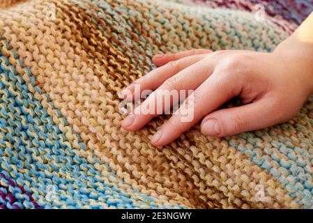 Die Hand der Frau liegt auf gestrickten mehrfarbigen Wolle handgefertigten Karo, Nahaufnahme, kreativen Hintergrund. Stockfoto