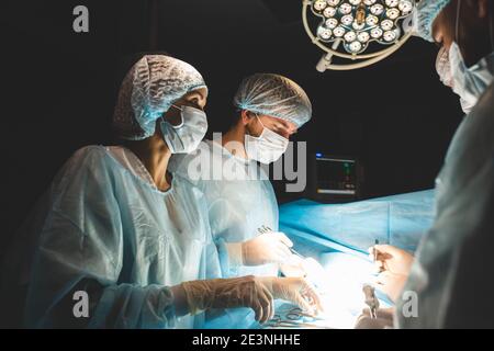Ein internationales Ärzteteam führt eine komplexe chirurgische Operation an einem unter Anästhesie stehenden Patienten durch. Moderner Operationssaal und erfahrene Chirurgen Stockfoto