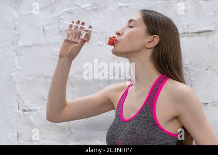 Junge Sportlerin Frau macht eine Pause Trinkwasser aus Plastikflasche. Junge Frau Trinkwasser nach dem Training in der Turnhalle, Gesundheit und Sport Stockfoto