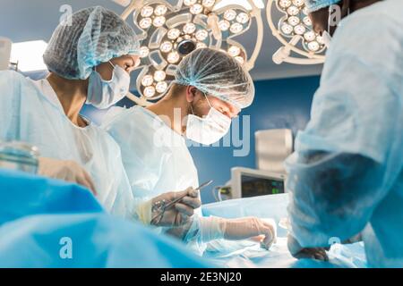 Ein internationales Ärzteteam führt eine komplexe chirurgische Operation an einem unter Anästhesie stehenden Patienten durch. Moderner Operationssaal und erfahrene Chirurgen Stockfoto
