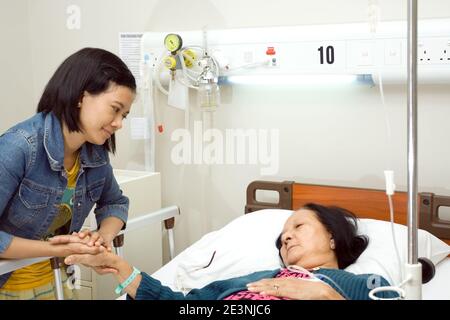 Eine südostasiatische Enkelin besucht ihre kranke Großmutter, die zur stationären Behandlung im Krankenhaus betritt Stockfoto