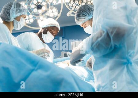 Ein internationales Ärzteteam führt eine komplexe chirurgische Operation an einem unter Anästhesie stehenden Patienten durch. Moderner Operationssaal und erfahrene Chirurgen Stockfoto