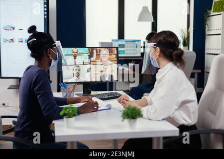 Afrikanischer Mitarbeiter und Manager diskutieren bei einer Videokonferenz mit Geschäftsleuten, die Gesichtsmaske tragen. Neues normales Geschäftsbüro. Multiethnisches Team, das während der globalen Pandemie mit Coronavirus soziale Distanz respektiert. Stockfoto