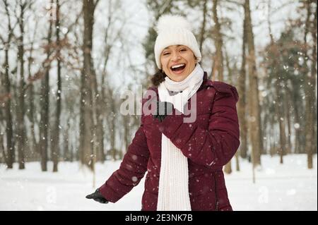 Outdoor-Foto von glücklichen Frau in weiß gestrickt Hut und Schal Spaß in verschneiten Morgen auf verschneiten Winterwald. Stockfoto