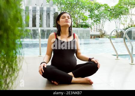 Schwangere südostasiatische Frau in Black Tank Top und Legging sitzend im Kreuz von Poolside tun Yoga-Übung für Gesundheit Stockfoto