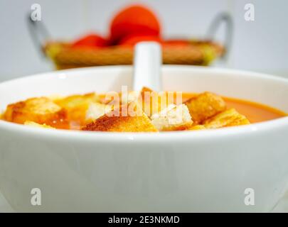 Schöne Aussicht auf Tomatensuppe mit Brotkronen in einem Schüssel mit Suppenlöffel und Tomaten in einem Korb in Der Hintergrund Stockfoto