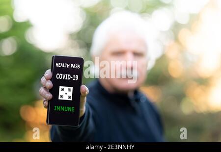 Älterer Mann, der einen Impfpass auf einem Mobiltelefon vorweist, der auf eine Impfung gegen covid-19 hinweist. Stockfoto