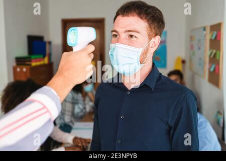 Frau, die die Körpertemperatur eines Mitarbeiters im modernen Büro misst - Fokus auf das Gesicht des Menschen Stockfoto