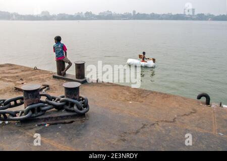 Ein kleiner Junge ist mit dem Floß auf dem Ganges in Kalkutta unterwegs. Reisen auf diesem Floß ist nur ein Teil der Kindheit. Stockfoto