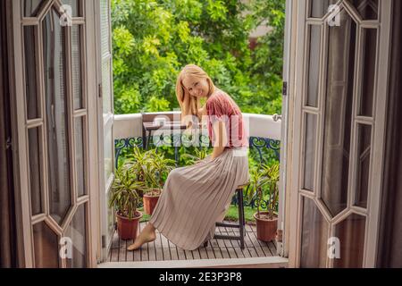 Eine rothaarige Frau steht auf einem Balkon im traditionellen Stil und genießt ihren Morgenkaffee. Eine Frau in einem Hotel in Europa oder Asien als Tourismus erholt sich von einem Stockfoto