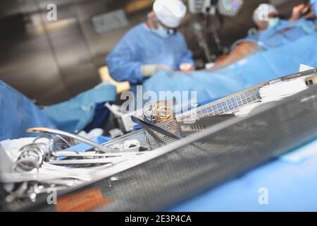 Sterile chirurgische Werkzeuge in der Schale auf dem Hintergrund der arbeitenden Chirurgen. Stockfoto