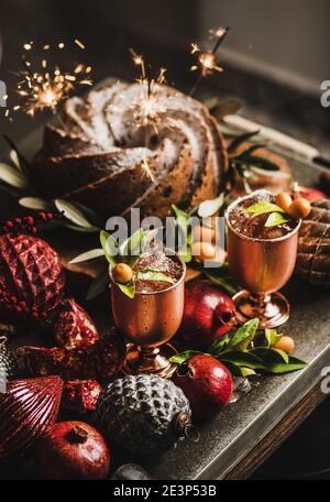 Weihnachts- oder Thanksgiving-Tag festlicher gebundener Kuchen mit Wunderkerzen und winterlichen Zitruscocktails in Kupferkelchen auf der Küchentheke. Winterferien festliche Stimmung Konzept Stockfoto