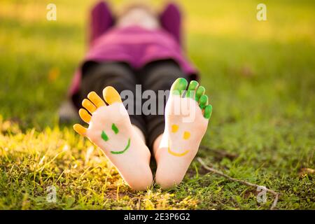 Kind Mädchen mit bemalten Fuß auf grünem Gras Spaß im Freien im Frühling Park. Stockfoto